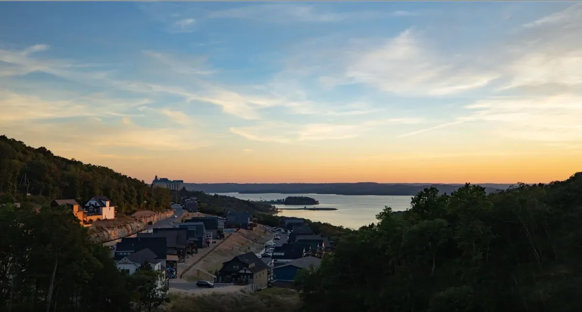 This serene landscape captures a tranquil sunset over the lake, with gently rolling hills and nearby houses visible along the shoreline. The calming mood and natural beauty evoke the outdoor adventures and scenic walks available to guests and their pets.