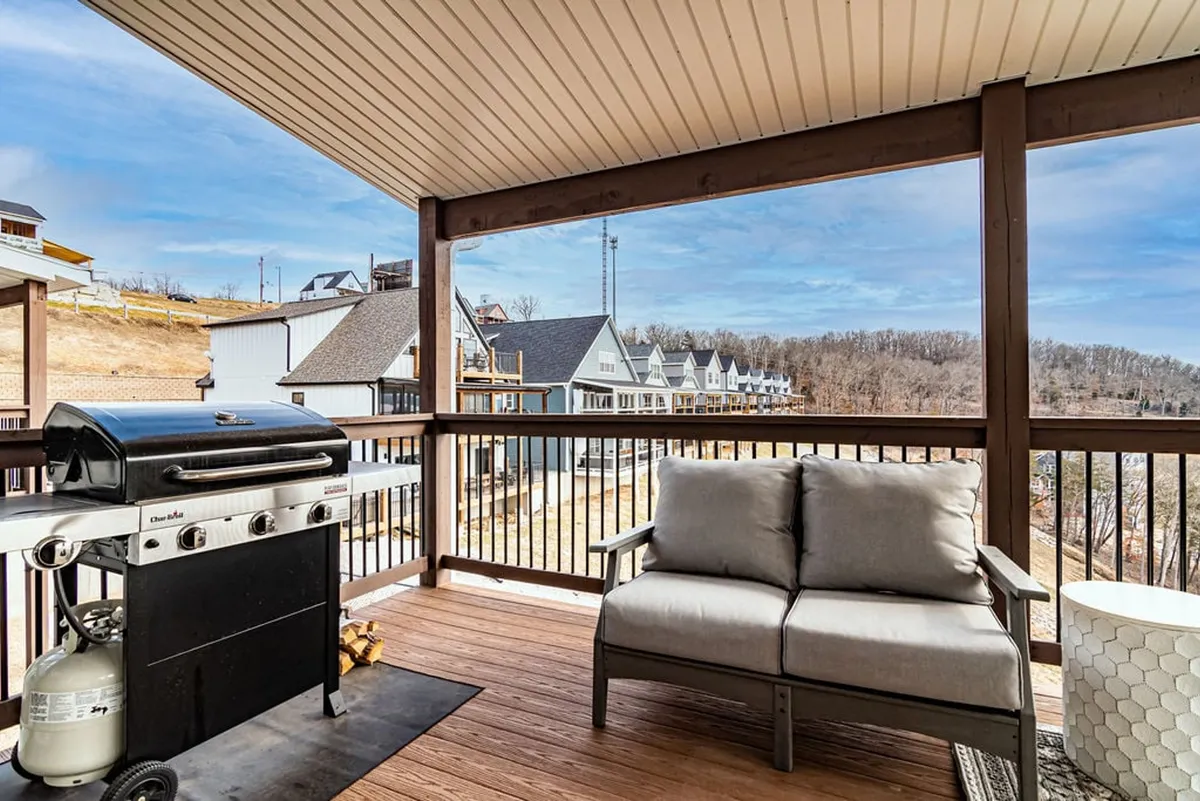 A lively exterior scene showcasing a grill and comfortable outdoor seating, with a view of surrounding homes under a colorful sky. The space is clearly set up for barbecuing, socializing, and enjoying the outdoors as a group.