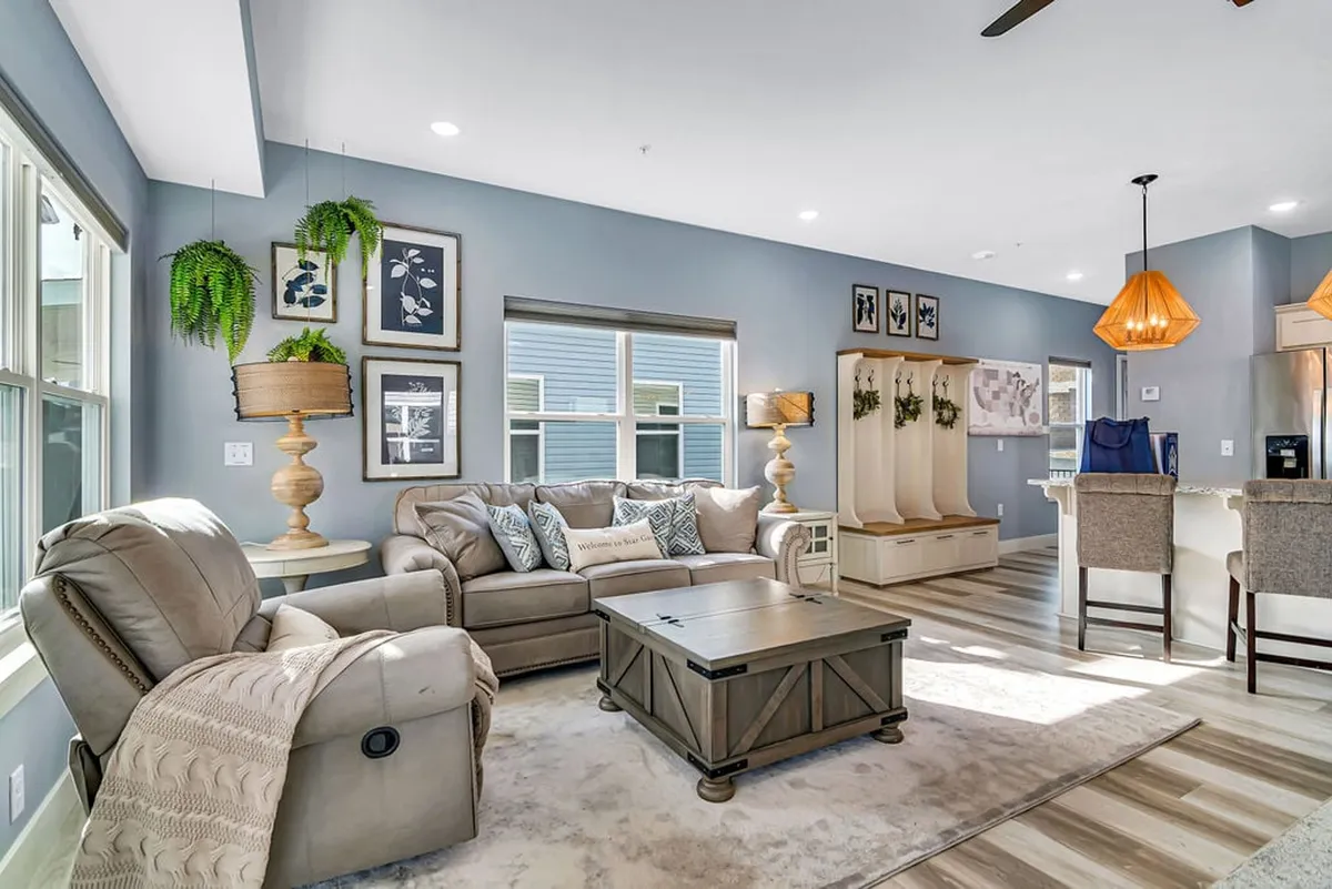 The image shows a warm, inviting living room with a plush sofa, stylish coffee table, modern lighting fixtures, tasteful wall art, and a handy entryway bench. The setup encourages socializing, relaxation, and family-friendly gatherings in a cozy atmosphere.