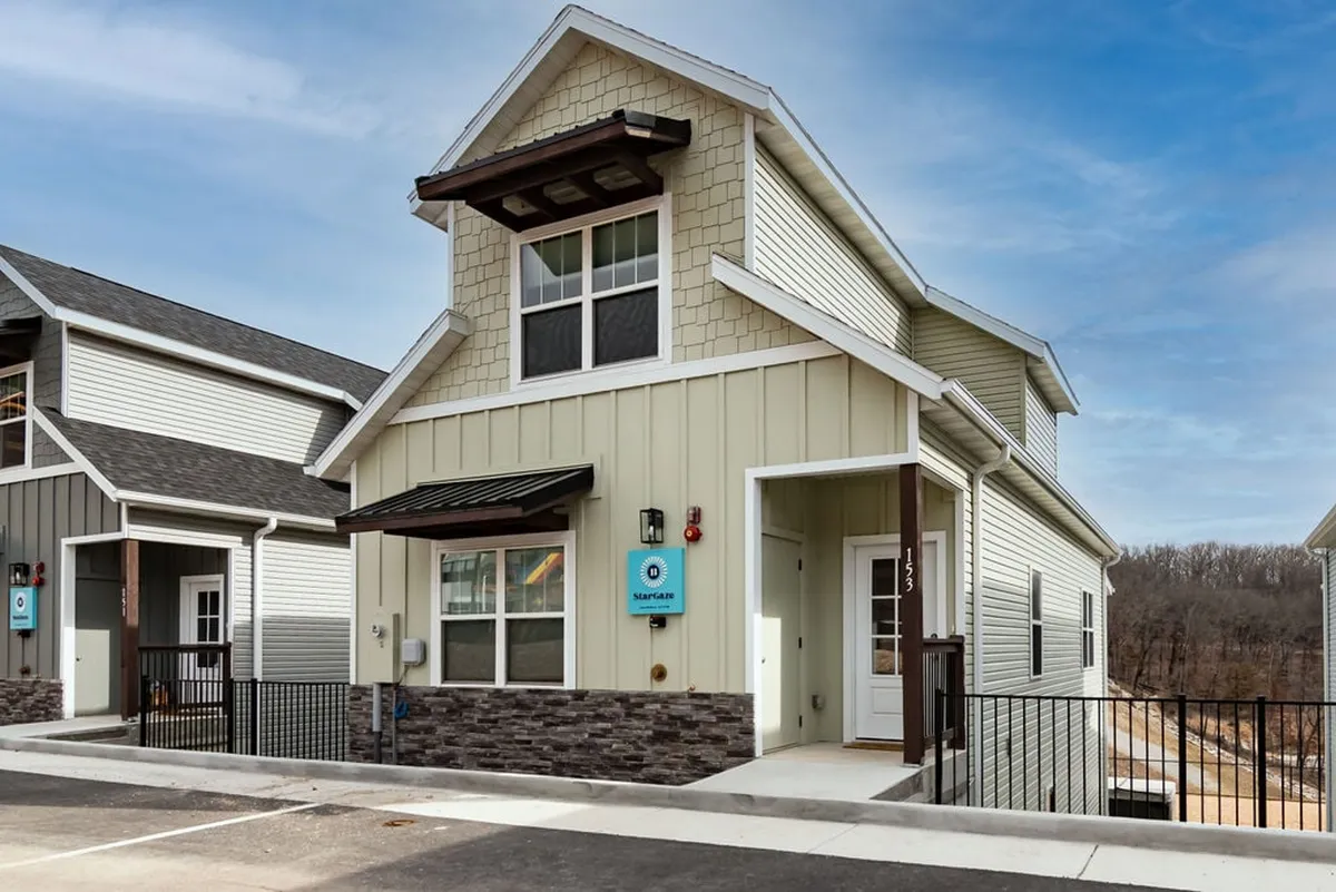 A view of the home's front entrance with a stone facade and unique roofline, offering a glimpse into the inviting neighborhood setting. The porch and landscaping subtly suggest a safe, walkable community environment, perfect for dog walks and outdoor exploration.