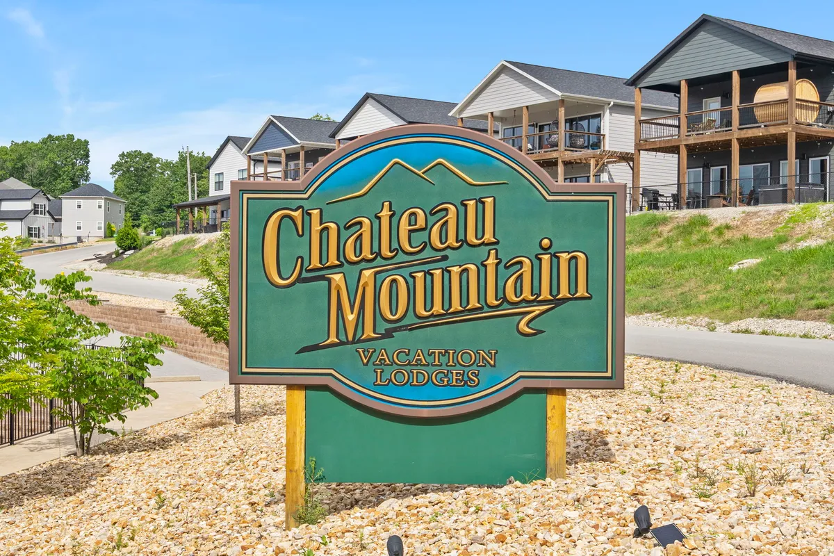 The image highlights the entrance to Chateau Mountain, with the property sign, nearby vacation lodges, and landscaped surroundings under a vast sky. The setting evokes a sense of arrival and communal exploration, hinting at adventure and group experiences.