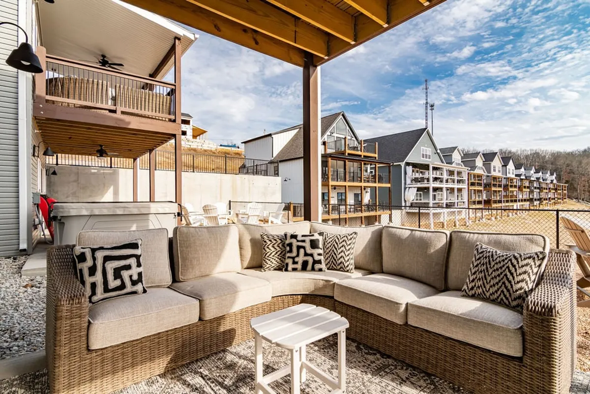 This image features a cozy outdoor sectional sofa with decorative pillows and a spacious dining area set in a fenced backyard. The inviting setup hints at a relaxed atmosphere ideal for entertaining or family time, with enough space for pets to roam safely. The fire pit area and surrounding greenery further emphasize the comfort and security of the outdoor space.