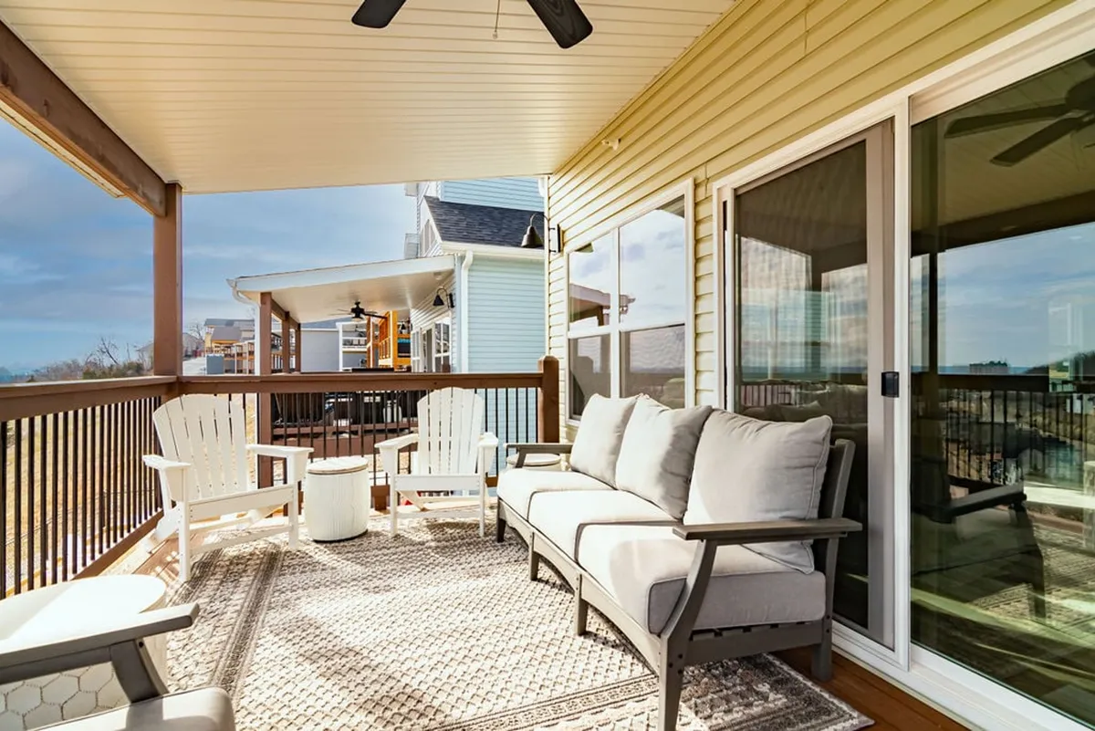 This image features an inviting outdoor seating area looking through glass doors onto a decorative rug, with hints of a beautiful sunset view. The setting is perfect for casual gatherings, outdoor meals, or relaxing with friends after a day of activities.